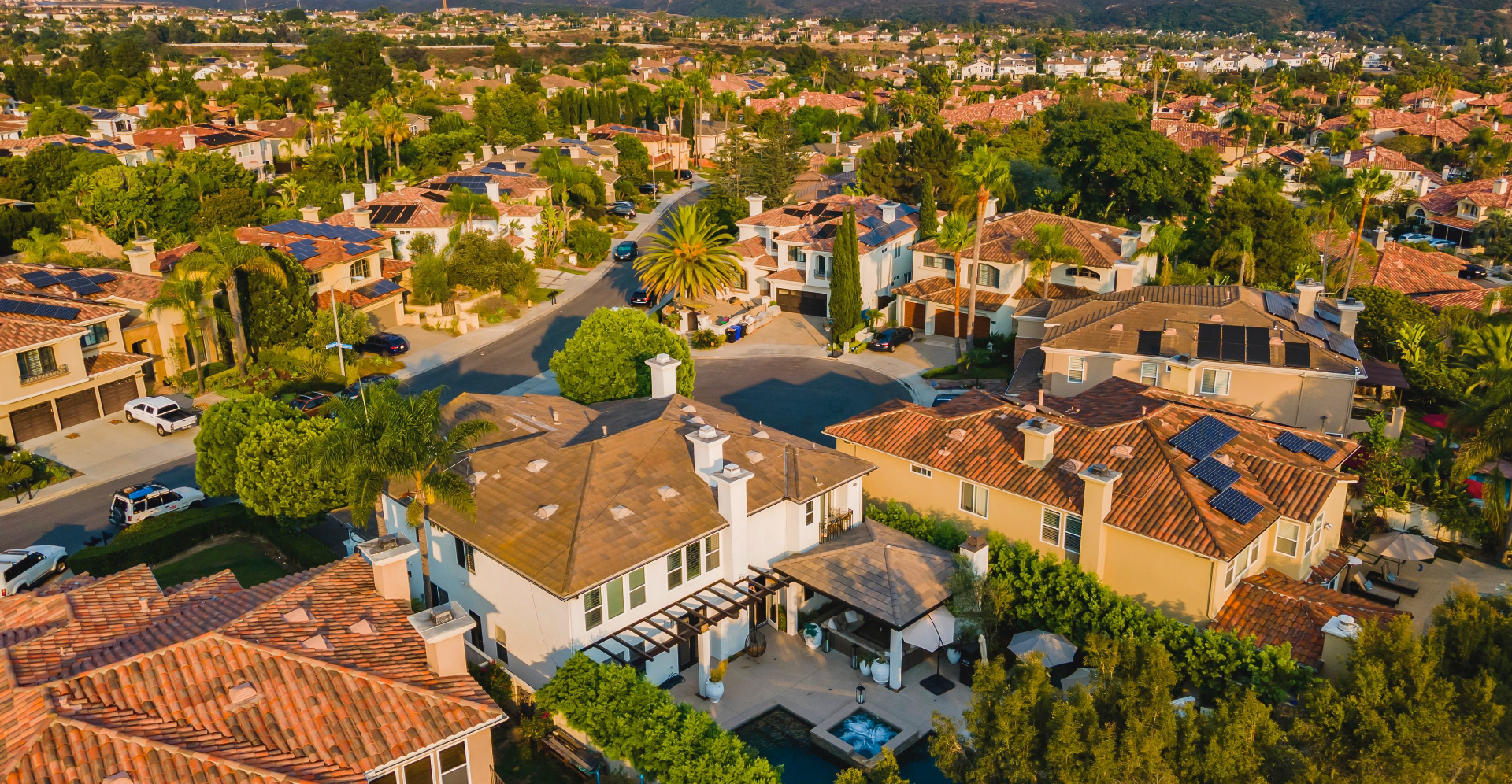 Aerial view of luxury homes in Carmel Valley, San Diego with terracotta rooftops, palm trees, and coastal hills at golden hour
