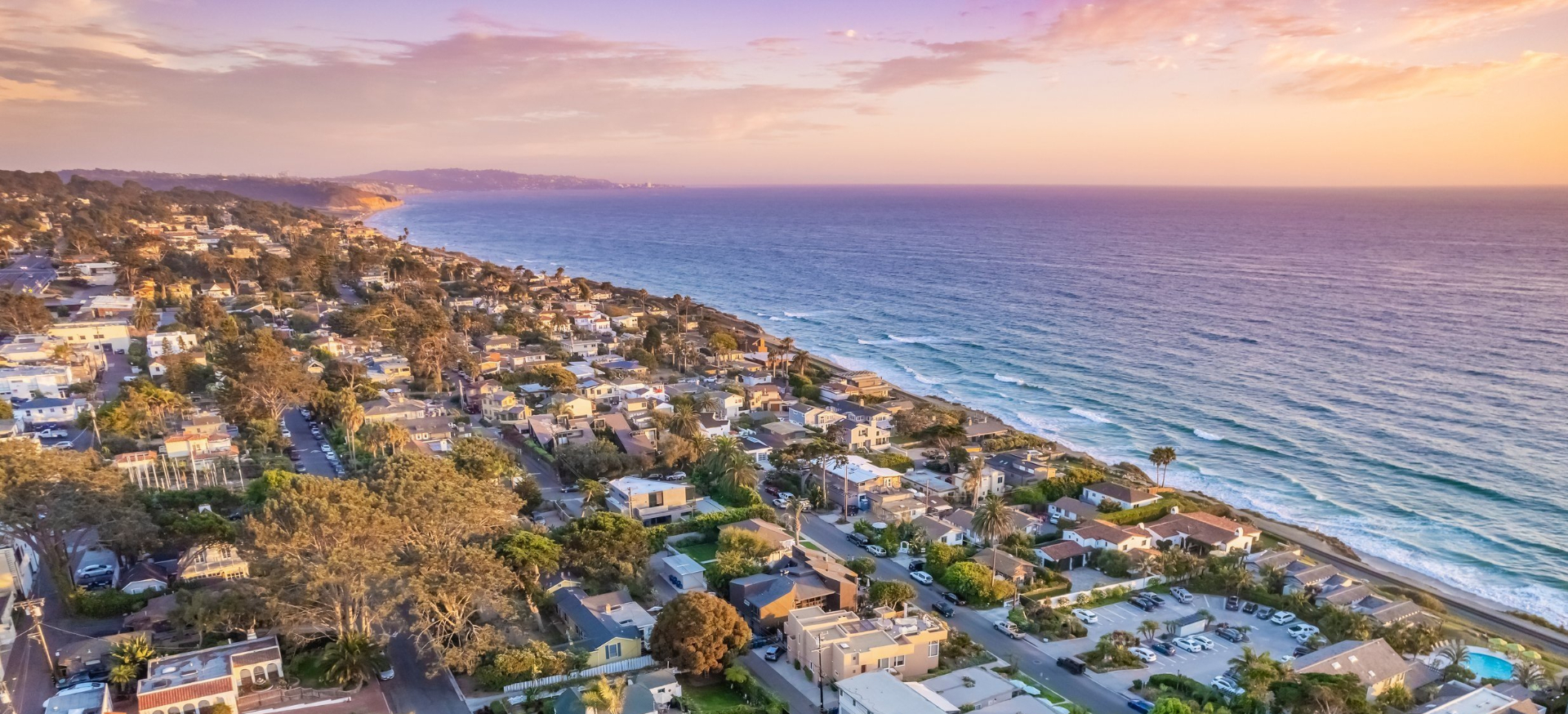 Aerial view of Del Mar, California coastline at sunset with oceanfront homes, the Pacific Ocean, and golden sky